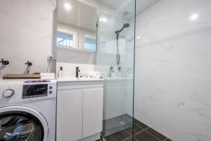 a white bathroom with a washer and a glass shower at Sublime Locale with Skyline Views from Courtyard in Sydney
