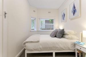 a white bedroom with a bed and two windows at Art Deco Apartment Meters Away From The Beach in Sydney