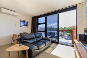 a living room with a leather couch and a large window at Gorgeous 2-Bed Apartment By Shops and the River in Batemans Bay