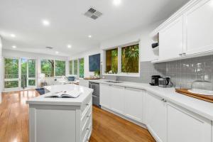 uma cozinha branca com bancadas brancas e janelas em Leafy Retreat with Deck & City Convenience em Sydney