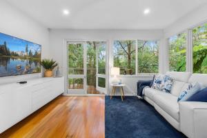 a living room with a white couch and large windows at Leafy Retreat with Deck & City Convenience in Sydney