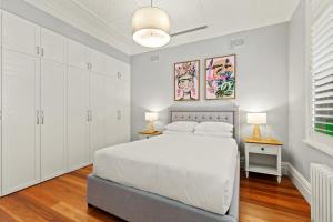 a white bedroom with a white bed and two lamps at Impeccably Chic 4-Bed Home with Spa & Pool in Sydney