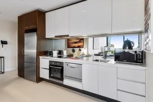 a kitchen with white cabinets and a stainless steel refrigerator at Chic Central Pad with City Views, Pool and Gym in Melbourne