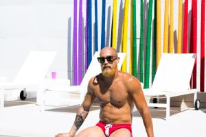 um homem sem camisa em calções de banho sentado numa praia em The Purple Hotel - Adults Only em San Antonio