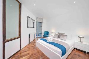 a white bedroom with a large bed and a blue chair at Oxford Circus Station Apartment- Mayfair! in London