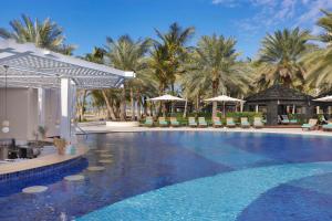 uma grande piscina com guarda-sóis e palmeiras em Waldorf Astoria Ras Al Khaimah em Ras al-Khaimah