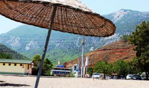 a straw umbrella on a beach with mountains in the background at Adrasan Shambala Hotel in Adrasan