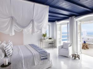 a white bedroom with a bed and a chair at Mykonos Blu, A Grecotel Resort to Live in Psarou +37 photos