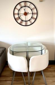 a glass table with two white chairs and a clock on the wall at Riverview Apartment in Dublin
