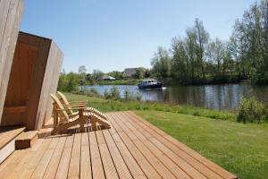 eine Holzterrasse mit zwei Stühlen und einem Boot auf einem Fluss in der Unterkunft Tiny house De Ljip in Westergeest
