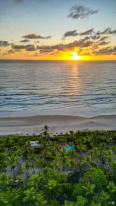 a sunset over the ocean with a beach with trees at Aldeia da Mata Ecolodge in Serra Grande