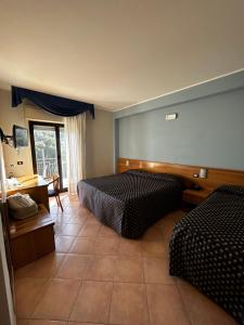 a bedroom with two beds and a desk and a window at Hotel Lachea in Acitrezza