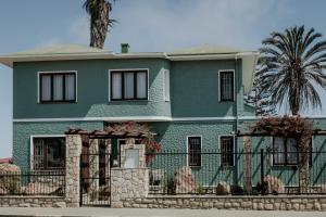 a green house with a fence and a palm tree at Fritz Manor Bed and Breakfast in Swakopmund