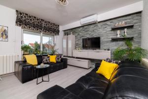 a living room with a black leather couch and yellow pillows at Apartmani Višnja in Crikvenica