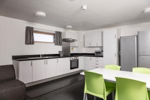 a kitchen with white cabinets and a table with green chairs at Wenlock Court in Luton