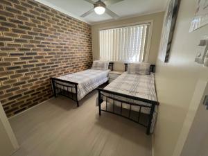 a room with two beds and a brick wall at Whispering Pines Unit 3, 7 Waratah Lane Evans Head in Evans Head