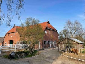 a large red brick barn with two horses in front of it at Kuschelige Ferienwohnung auf Reiterhof 