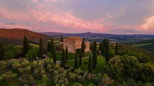 un edificio en una colina con árboles y una puesta de sol en Castello Di Vicarello en Sasso dʼOmbrone