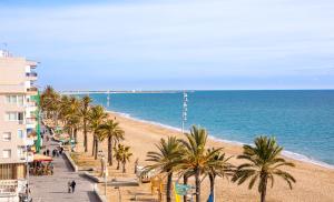 a beach with palm trees and a building and the ocean at 3 bedrooms appartement at Calafell 5 m away from the beach with sea view terrace and wifi in Calafell