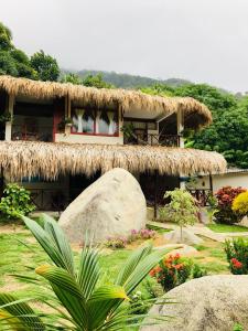 a building with a straw roof and a large rock at Hotel talú tayrona in El Zaino