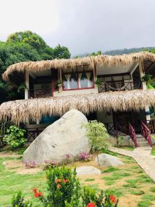 a house with a straw roof and a large rock at Hotel talú tayrona in El Zaino