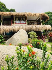 uma casa com telhado de palha e um jardim com flores em Hotel talú tayrona em El Zaino