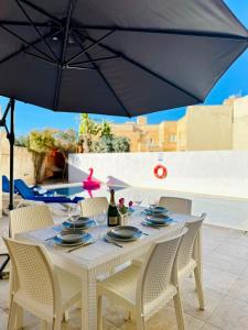 a white table with chairs and a black umbrella at Dawlet ix-Xemx Gozo Farmhouse in Kerċem