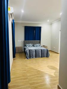 Schlafzimmer mit einem Bett mit blauen Vorhängen und Holzboden in der Unterkunft Short And Long Stay Six Bedroom Apartment in Tema