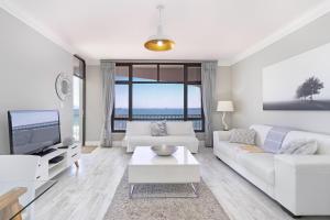 a living room with a white couch and a tv at Witsand 804 by Host Agents in Bloubergstrand