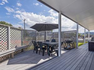 a deck with a table and chairs and an umbrella at Beach Life - Whangamata Holiday Home in Whangamata