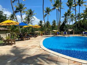 a swimming pool with chairs and umbrellas and palm trees at Chalé Centro, Praia Pipa in Pipa