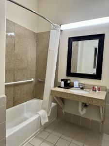 a bathroom with a tub and a sink and a mirror at Baymont by Wyndham Galveston in Galveston