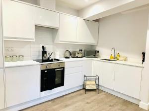 a white kitchen with white cabinets and a black oven at Margate Spacious Apartment - 5 min walk to beach in Margate