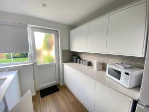 a kitchen with white cabinets and a microwave at Cosy Retreat In Royal Sutton Coldfield Close to Good Hope Hospital the NEC and Birmingham Airport in Birmingham
