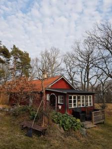 una piccola casa rossa con una panchina davanti di Ekbacken - naturskön stuga med närhet till havet a Nyköping
