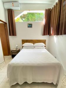a bedroom with a large white bed with a window at CHALÉ da LÚ ILHABELA in Ilhabela