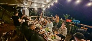 un grupo de personas sentadas en una mesa comiendo comida en Nhà Bên Suối - Homestay & Camping, en Da Lat