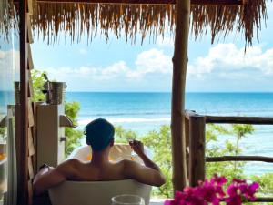 a man sitting in a chair with a glass of wine looking at the ocean at The Korowai in Uluwatu
