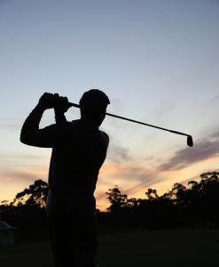 a man swinging a golf club with the sunset in the background at The Victoria Golf Club in Melbourne