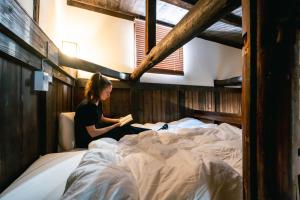 Eine Frau, die auf einem Bett sitzt und ein Buch liest. in der Unterkunft すずめや築地 in Tokio