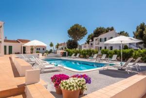 a swimming pool with chairs and umbrellas and flowers at Apartamentos Annabel's 2-3 HABITACIONES in Cala Galdana