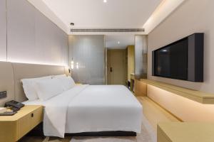 um quarto com uma cama branca e uma televisão de ecrã plano em Maans Hotel - Shenzhen University Science Park em Shenzhen