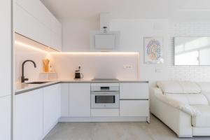 a kitchen with white cabinets and a white couch at Albir Playa in L’Alfàs del Pi