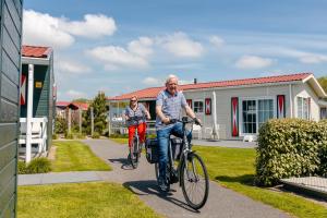 a man and woman riding bikes in front of a house at Strandcamping Valkenisse in Biggekerke