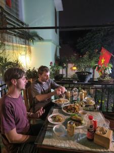 Dois homens sentados numa mesa com pratos de comida. em Tam Coc Lotus Flower Homestay em Ninh Binh
