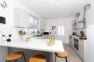a white kitchen with a white counter and wooden chairs at 5 Double Bedrooms with Ensuites - Teesside House TSAC in Redcar