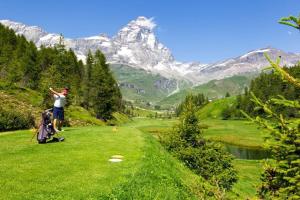 a man standing on a golf course with mountains in the background at FAIRWAY LODGE in Breuil-Cervinia