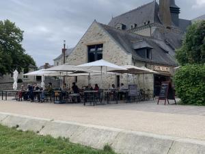 mensen aan tafels met parasols voor een gebouw bij Grande Maison Cosy Proche Angers & Bords de Loire in Bouchemaine