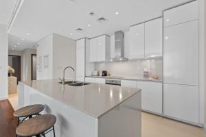 a white kitchen with white cabinets and stools at Brand New Spacious 2 Beds City Walk B9 in Dubai