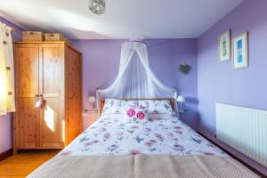 サルタッシュにあるWheel Cottage, Landrakeの紫の壁のベッドルーム1室、ピンクのバラ2本が飾られたベッド1台が備わります。